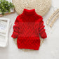 Enfant souriant portant un pull en tricot torsadé rouge