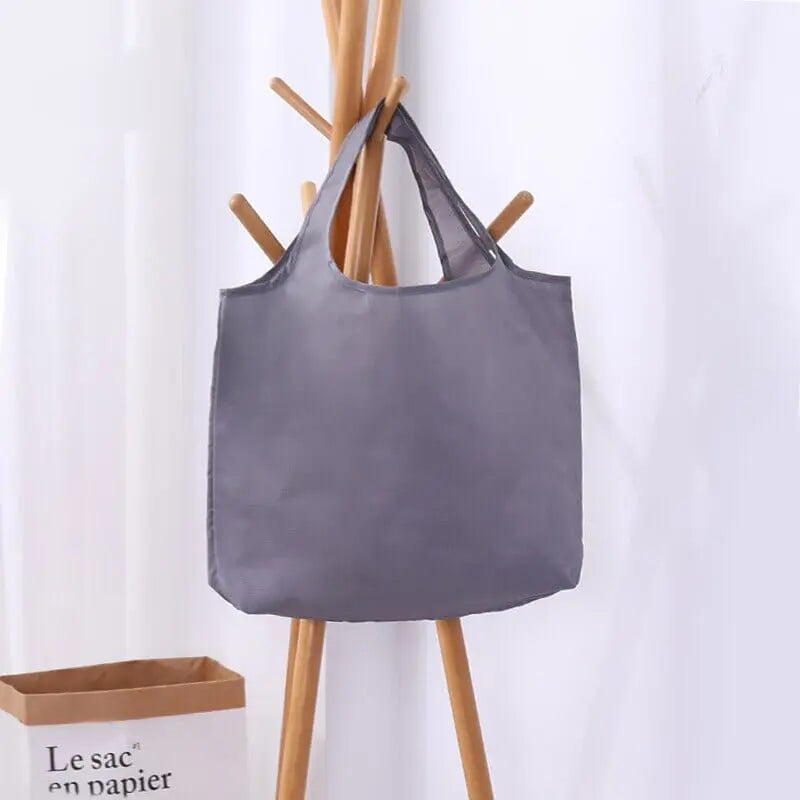 Sac de voyage gris, plié et compact, sur une surface blanche